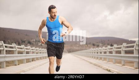 Ein Mann, der auf einer Brücke läuft und auf seine Smartwatch schaut Stockfoto