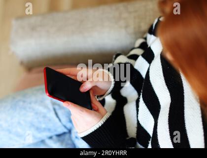 Ein Foto von einem Mädchen, das ein Smartphone mit leerem Bildschirm im Zimmer hält Stockfoto