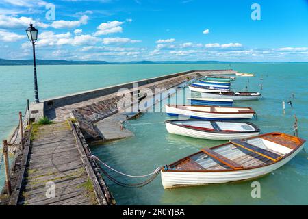 Holzpier in Balatonlelle mit bunten Booten auf dem blauen Himmel und Wasser des Balaton-Sees Stockfoto