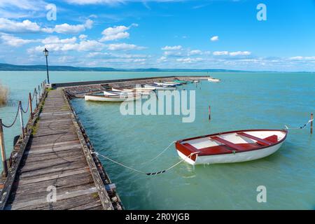 Holzpier in Balatonlelle mit bunten Booten auf dem blauen Himmel und Wasser des Balaton-Sees Stockfoto