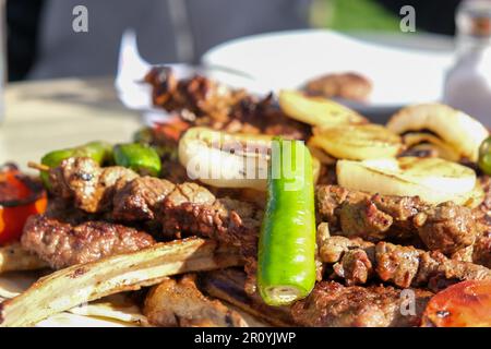 Nahaufnahme köstliches gemischtes Kebab Fleisch Chopsteak Fleischklößchen Spießerlamm mit Gemüse Pfeffer Tomaten Zwiebeln in der Nähe des Brots. Selektiver Fokus des Bereichs. Stockfoto