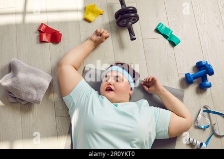 Lustige, müde, faule, dicke Frau, die auf dem Boden zwischen den Geräten für Sport-Workout schläft Stockfoto