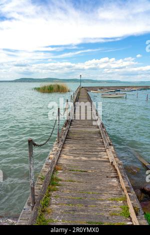 Hölzerner Pier in Balatonlelle mit bunten Booten auf dem blauen Himmel und dem Wasser des Balaton. Stockfoto