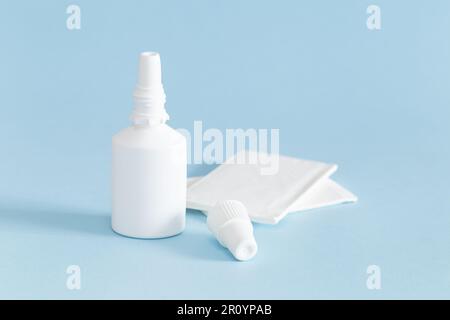 Eine Flasche Nasenspray mit entferntem Stopfen und weißem Papiertaschenpapier auf blauem Hintergrund. Stockfoto