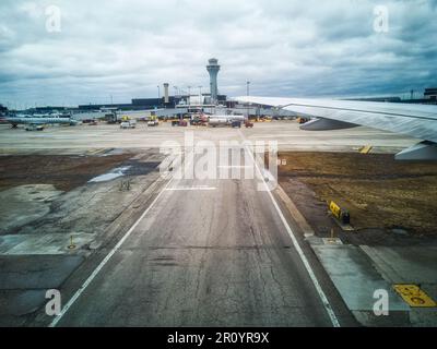 Ein Blick aus einem Flugzeugfenster auf eine kommerzielle Start- und Landebahn des Flughafens, mit einem großen Flugzeug im Vordergrund Stockfoto