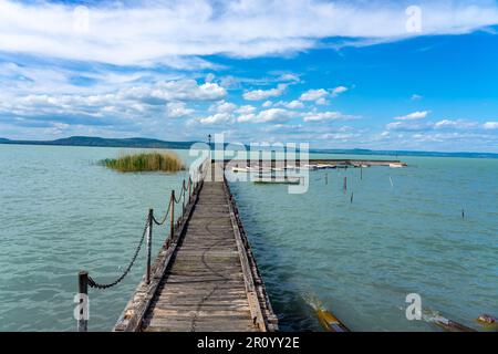 Hölzerner Pier in Balatonlelle mit bunten Booten auf dem blauen Himmel und dem Wasser des Balaton. Stockfoto