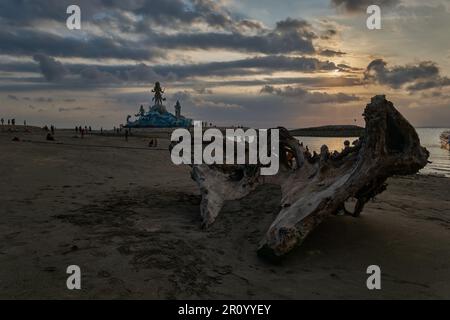 Pantai Jerman (deutscher Strand) in Kuta, Bali Indonesien bei Sonnenuntergang mit der Statue von Varuna (der Gott des Himmels, des Wassers und des Ozeans), während Menschen zu Fuß unterwegs sind Stockfoto