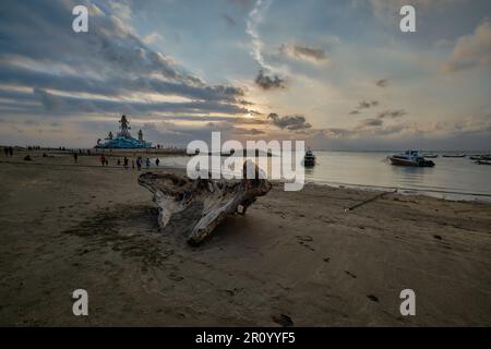 Pantai Jerman (deutscher Strand) in Kuta, Bali Indonesien bei Sonnenuntergang mit der Statue von Varuna (der Gott des Himmels, des Wassers und des Ozeans), während Menschen zu Fuß unterwegs sind Stockfoto