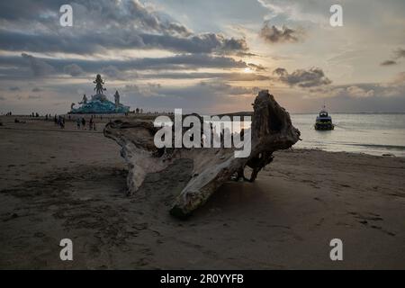 Pantai Jerman (deutscher Strand) in Kuta, Bali Indonesien bei Sonnenuntergang mit der Statue von Varuna (der Gott des Himmels, des Wassers und des Ozeans), während Menschen zu Fuß unterwegs sind Stockfoto