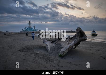 Pantai Jerman (deutscher Strand) in Kuta, Bali Indonesien bei Sonnenuntergang mit der Statue von Varuna (der Gott des Himmels, des Wassers und des Ozeans), während Menschen zu Fuß unterwegs sind Stockfoto