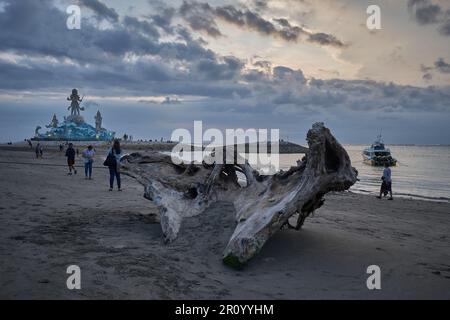 Pantai Jerman (deutscher Strand) in Kuta, Bali Indonesien bei Sonnenuntergang mit der Statue von Varuna (der Gott des Himmels, des Wassers und des Ozeans), während Menschen zu Fuß unterwegs sind Stockfoto