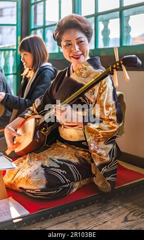 nagasaki, kyushu - 14 2022. dez.: Schammachtes Instrument, Demonstration mit Touristen durch eine japanische Frau im Kimono, die in einer traditionellen Seiza-Pose in t sitzt Stockfoto