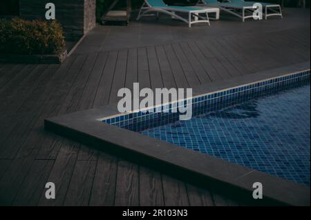 Eine Außenterrasse mit zwei Rasenstühlen neben einem schimmernden Swimmingpool Stockfoto