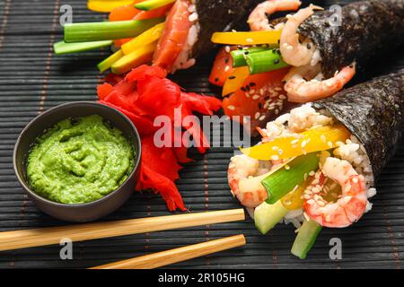 Bambusmatte mit leckeren Sushi-Zapfen, Ingwer und Wasabi, Nahaufnahme Stockfoto