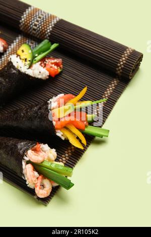 Bambusmatte mit leckeren Sushi-Zapfen auf farbigem Hintergrund, Nahaufnahme Stockfoto