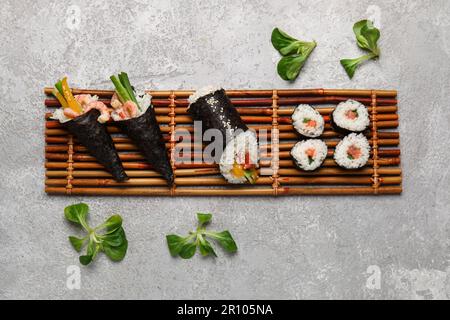 Bambusmatte mit leckeren Sushi-Zapfen, Brötchen und Lammsalat auf Grunge-Hintergrund Stockfoto