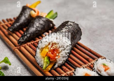 Bambusmatte mit leckeren Sushi-Rollen und Zapfen auf Grunge-Hintergrund, Nahaufnahme Stockfoto