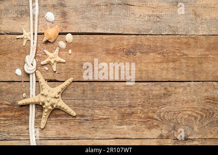 Muscheln und Seesterne mit Seil auf braunem Holzhintergrund Stockfoto