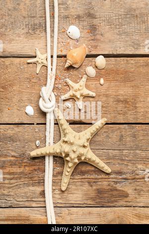 Muscheln und Seesterne mit Seil auf braunem Holzhintergrund Stockfoto