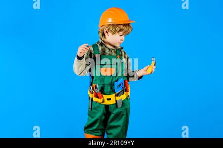 Junge mit Schutzhelm und Werkzeuggürtel mit Hammer. Kind in Baukleidung mit Werkzeugen zur Reparatur. Kleiner Handwerker oder Bauarbeiter Stockfoto