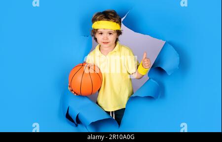 Kind in Sportbekleidung mit Basketballball mit Daumen nach oben. Basketballtraining. Sportspiel. Aktiver Sport-Lifestyle. Kleiner Basketballer mit Stockfoto