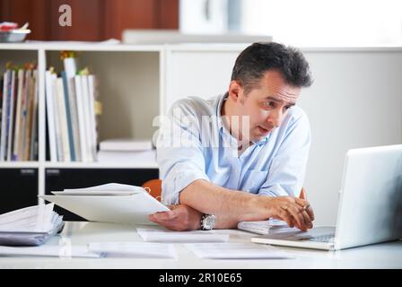 Lange Arbeitszeiten fordern ihren Tribut... ein reifer Büroangestellter sieht müde aus, wenn er an seinem Schreibtisch arbeitet. Stockfoto