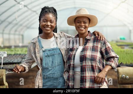Porträt zweier Landarbeiter. Glückliche Kollegen, die sich in ihrem Garten umarmen. Lächelnde Kollegen, die zusammen in ihrem Garten stehen. afroamerikaner Stockfoto