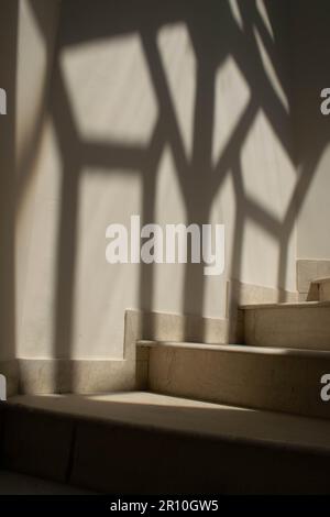 Wendeltreppe aus weißem Marmor und einem wunderschönen künstlerischen diamantförmigen Schatten an der Wand an der Seite der Treppe oder im Hintergrund. Stockfoto