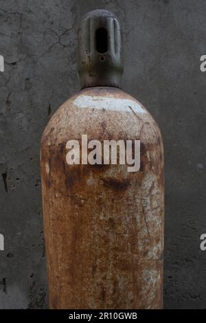 Gruselig aussehende verlassene rostige, schimmelige und alte Gasflasche für den Kühlschrank vor der strukturierten alten Wand. Stockfoto