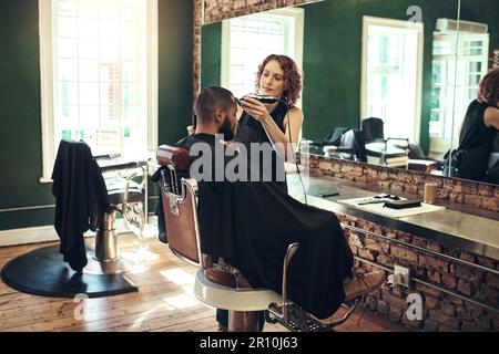 Veränderung schafft Vertrauen. Eine attraktive, junge Friseurin, die ihre Kunden im Salon frisiert. Stockfoto