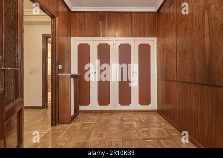 Ein leerer Raum mit holzgetäfelten Wänden und einem eingebauten Kleiderschrank mit weißen und braunen Holztüren Stockfoto