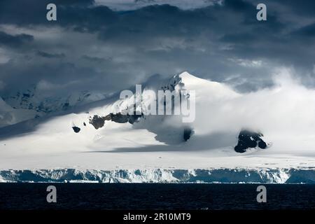 Stürmische Wolken überqueren Berge in antarktischen Eisbergen an der Küste, Wind, Schnee und dunkler Himmel. Stockfoto