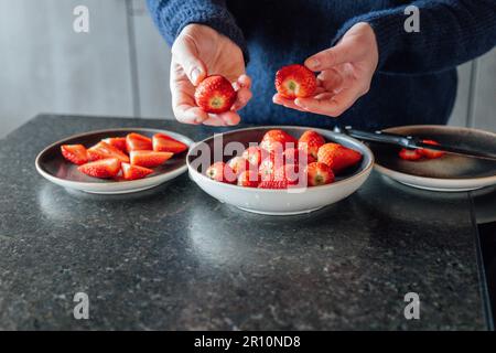 Erdbeeren schneiden. Frühstückszubereitung. Die Hände schneiden frische Erdbeeren und legen einen Teller rein. Erdbeeren zum Servieren vorbereiten. Frau schneidet Stockfoto