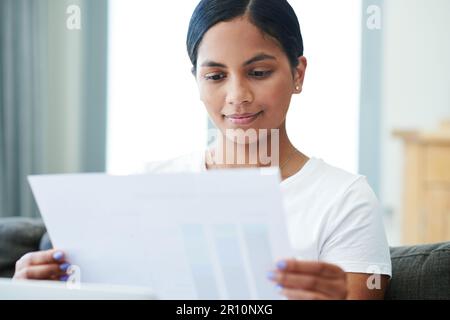 Die Budgets scheinen alle in Ordnung zu sein. Eine attraktive junge Frau, die allein auf ihrem Sofa zu Hause sitzt und ihre Finanzen kalkuliert. Stockfoto