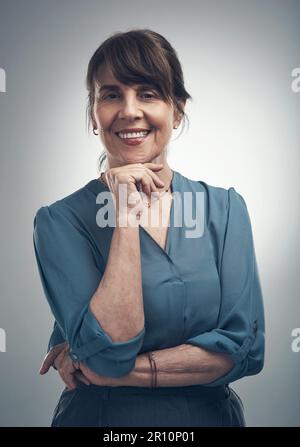 Ich komme immer im Vertrauen gekleidet. Studioporträt einer Seniorin, die mit der Hand am Kinn posiert, vor grauem Hintergrund. Stockfoto