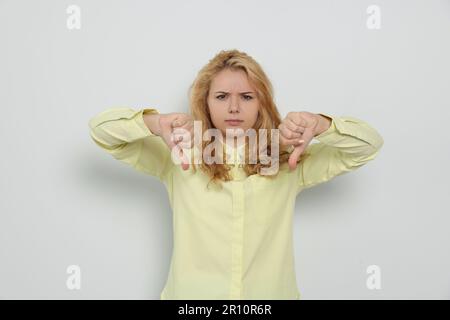 Unzufriedene junge Frau mit Daumen nach unten auf weißem Hintergrund Stockfoto