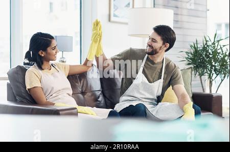 Eine starke Partnerschaft zahlt sich aus. Ein glückliches, junges Paar, das sich gegenseitig einen High Five gibt, nachdem es ihr Zuhause zusammen geputzt hat. Stockfoto