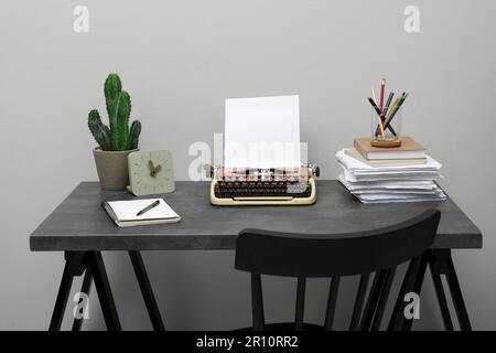 Schreibmaschine und Papierstapel auf einem dunklen Tisch nahe der hellgrauen Wand. Schreibarbeitsplatz Stockfoto