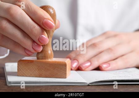 Ukraine, Lemberg - 6. September 2022: Frau stempelt Visumseite im Reisepass am Holztisch ab, Nahaufnahme Stockfoto