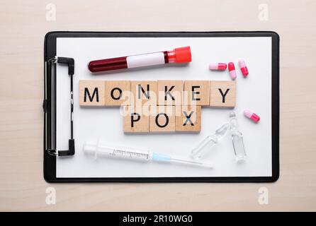 Flache Laienzusammensetzung mit den Wörtern Affen Pocken aus Quadraten und Reagenzglas auf Holztisch Stockfoto