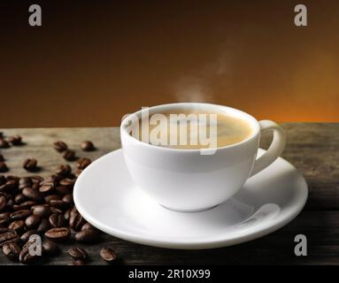 Tasse heißen aromatischen Kaffees und geröstete Bohnen auf einem Holztisch vor braunem Hintergrund Stockfoto