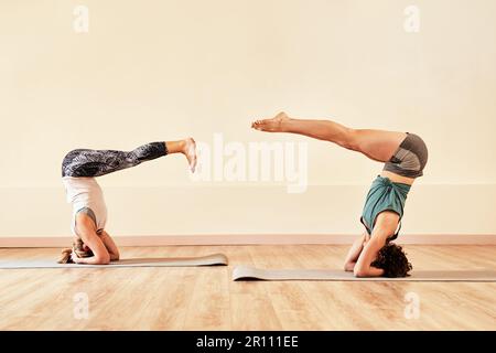 Nichts verändert deine Sicht auf das Leben so gut wie Yoga. Zwei junge Frauen, die in einem Yoga-Kurs Kopfständer machen. Stockfoto