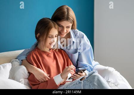 Positiv, dass mutter und Tochter zusammen im Bett zu Hause ein Video auf einem Smartphone ansehen. Stockfoto