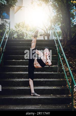 Tanzkünstlerin, die Akrobatik und Flexibilität in Absätzen macht. Tanzmädchen, das auf der Treppe draußen flexibel ist. Porträt einer Tänzerin in Fersen Stockfoto