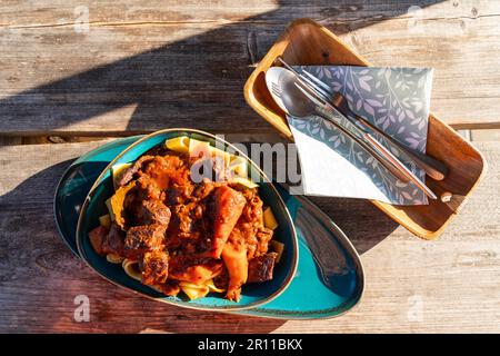 Gulasch mit Nudeln und Besteck auf einem Holztisch, Landgasthof zum Gruenen Baum, Dorf Ringenwalde, Uckermark, Brandenburg, Deutschland Stockfoto