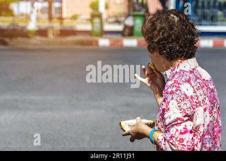 Rückblick auf eine ältere asiatische Frau, die gerne süße Durianfrucht in ihrer Hand am Straßenrand isst. Die alte Dame kaufte eine Durianfrucht und aß frische Durianfrucht Stockfoto