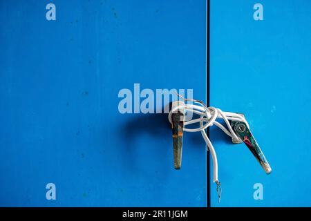 Bruchstücke weißer Elektrokabel wurden an silberne Knöpfe von Stahlschranktüren gebunden. Alte Tür mit Elektrokabel verriegelt. Blaues Schließfach mit o verriegelt Stockfoto