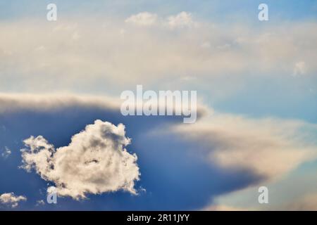 Ein Bild einer kleinen Wolke, beleuchtet von der Sonne, mit dunkleren Wolken im Hintergrund. Stockfoto