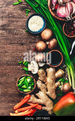 Asiatische Küche mit Gemüse, Essenshintergrund. Ingwer, Limette, Chili, Knoblauch, Sojasoße, Pilze, Paprika, grüne Zwiebeln auf Holz Stockfoto