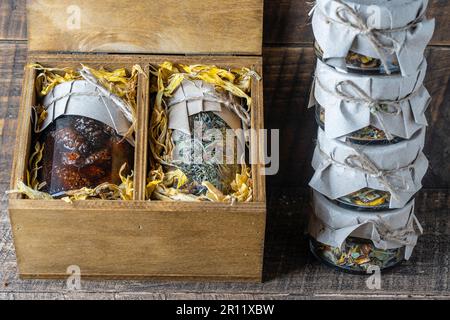 Glasbecher mit Blumentee und Glasbecher mit Kiefernkonfitüre in einer hölzernen Geschenkbox auf einem Tisch, Nahaufnahme. Schönes Geschenk für Familie und Freunde Stockfoto